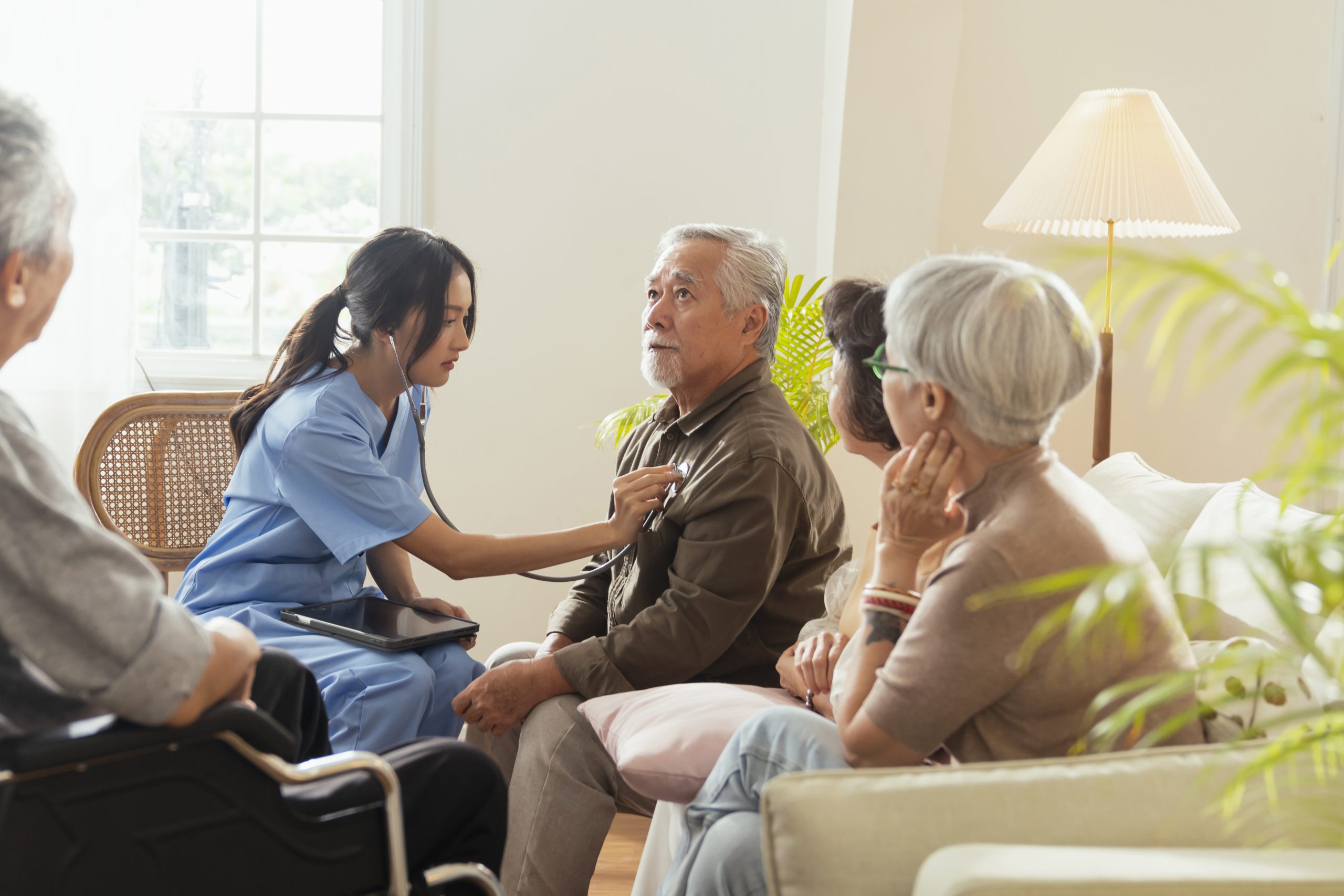 happiness Cheerful elderly woman and men talking with female caregiver nurse doctor having health checking consult at living area,Caretakers with senior couple sitting in living room at nursing home